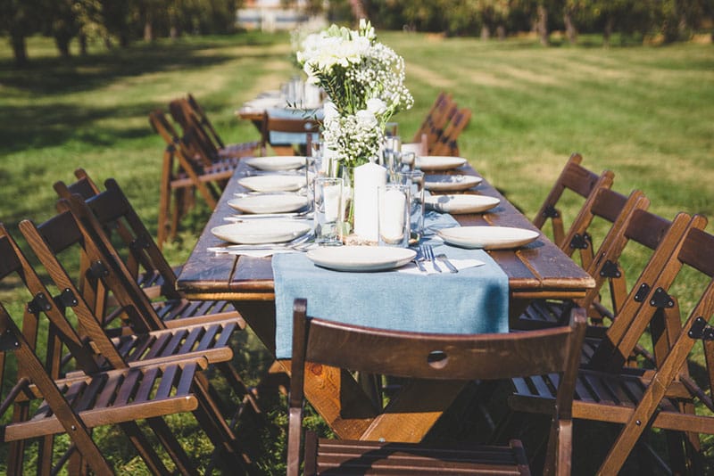 Tafel buiten met houten stoelen en gedekt met witte bloemen en borden